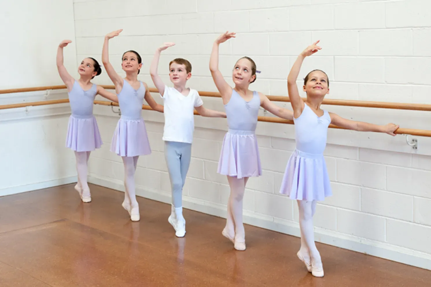 Young ballet students in lavender leotards practising arm positions at the barre at Mathis Dance Studios