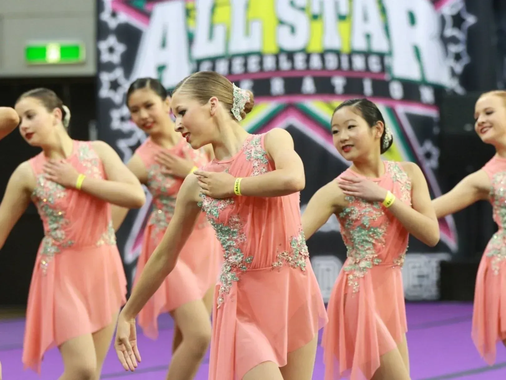 Cheerleaders in peach dresses with sparkling accents performing a choreographed routine at a competition.