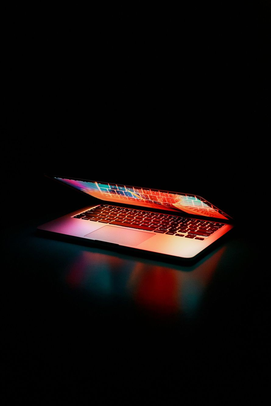 A laptop computer is open and sitting on a table in the dark.