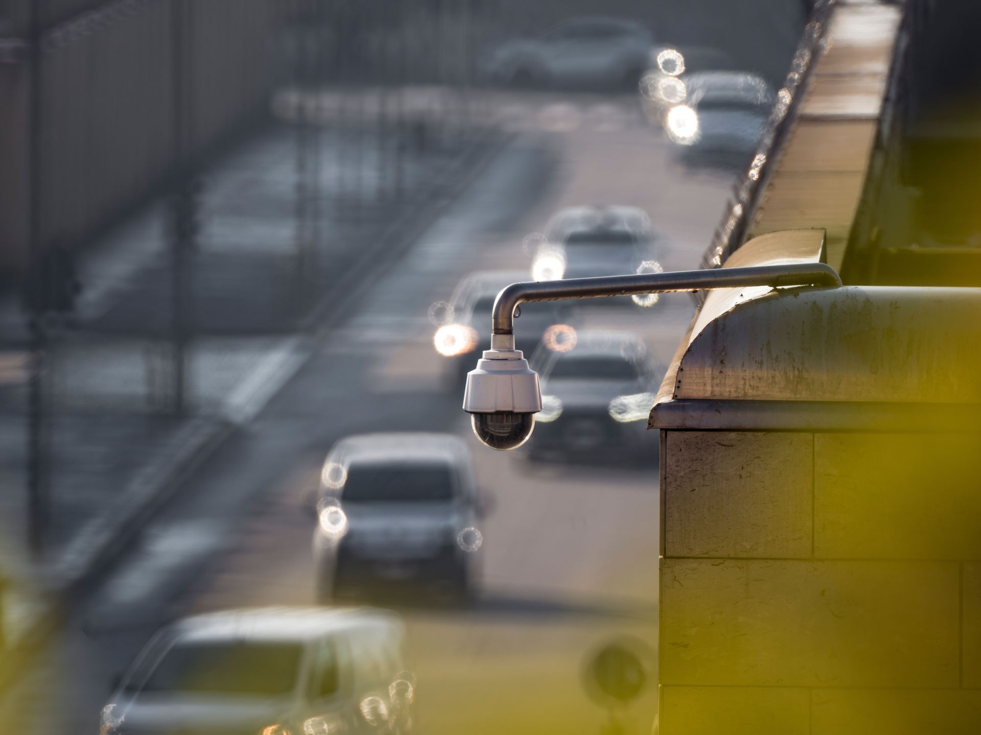 Security camera mounted on a bridge overlooking blurred traffic on a highway