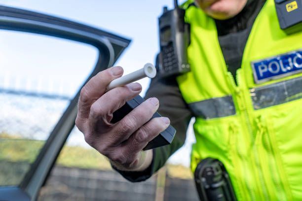 Police officer in high-visibility vest holding a breathalyzer beside an open car door