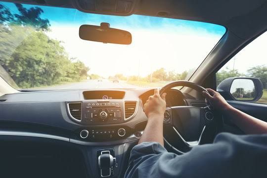 Driver holding the steering wheel on a sunlit road, seen from inside a car