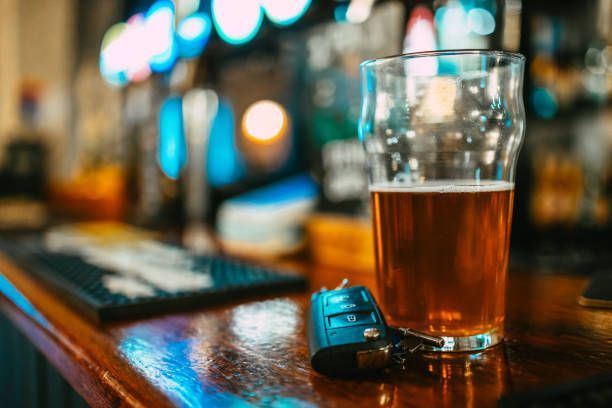 Beer glass and car keys on a bar counter with blurred lights in the background