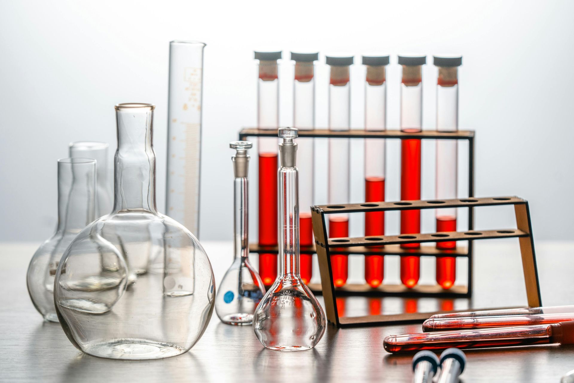 Assorted laboratory glassware with red liquid in test tubes on a reflective surface