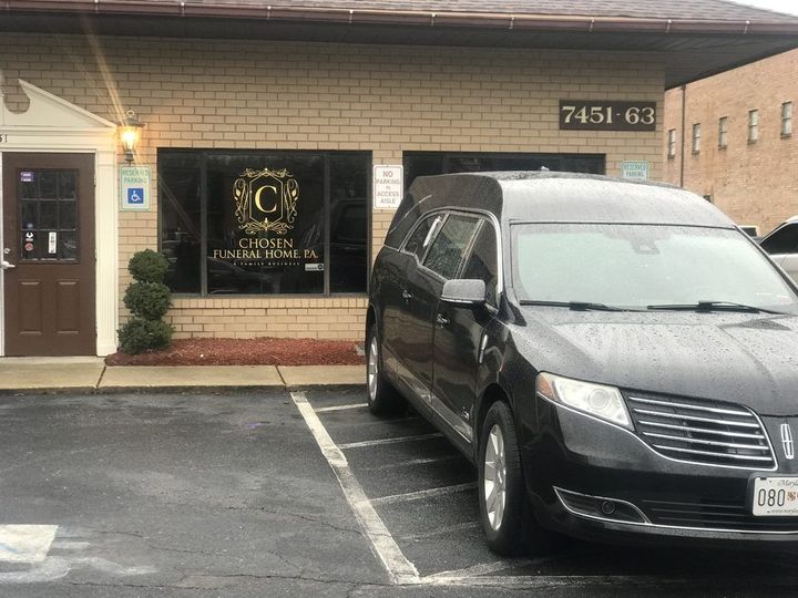 A black hearse parked in front of a brick business building with a gold 