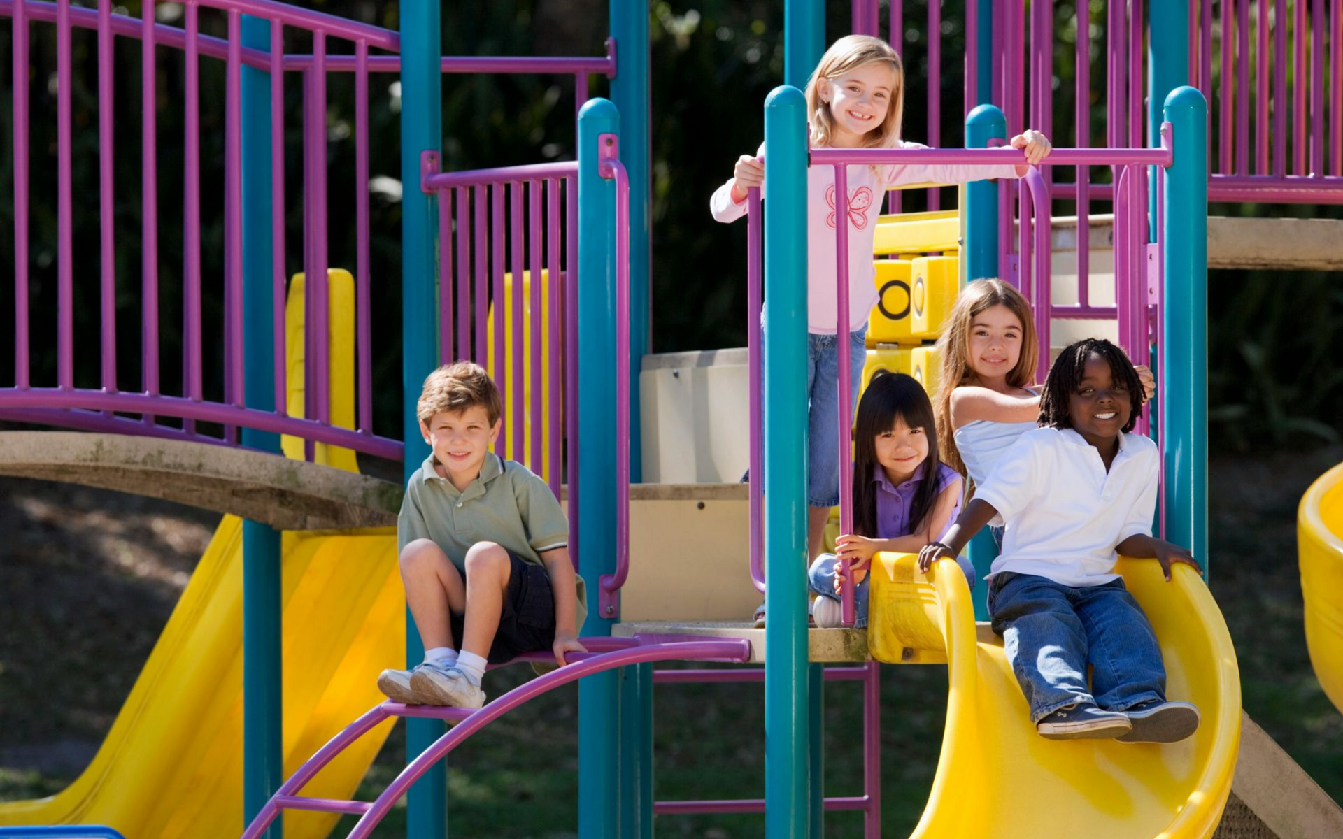 Children playing on a colorful playground slide and climbing structure.