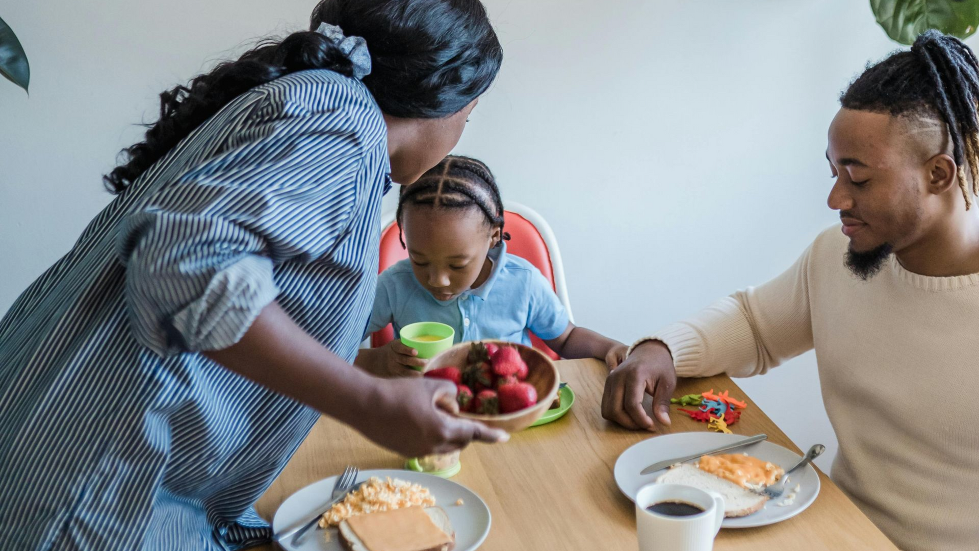Family sharing a meal at a table, with adults serving a child and plates of food visible.