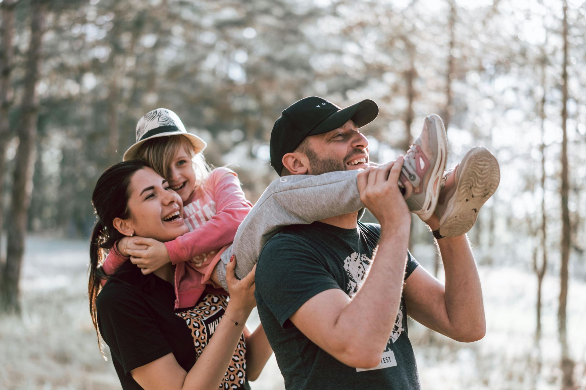 A family outdoors, smiling as one carries a child on their shoulders.