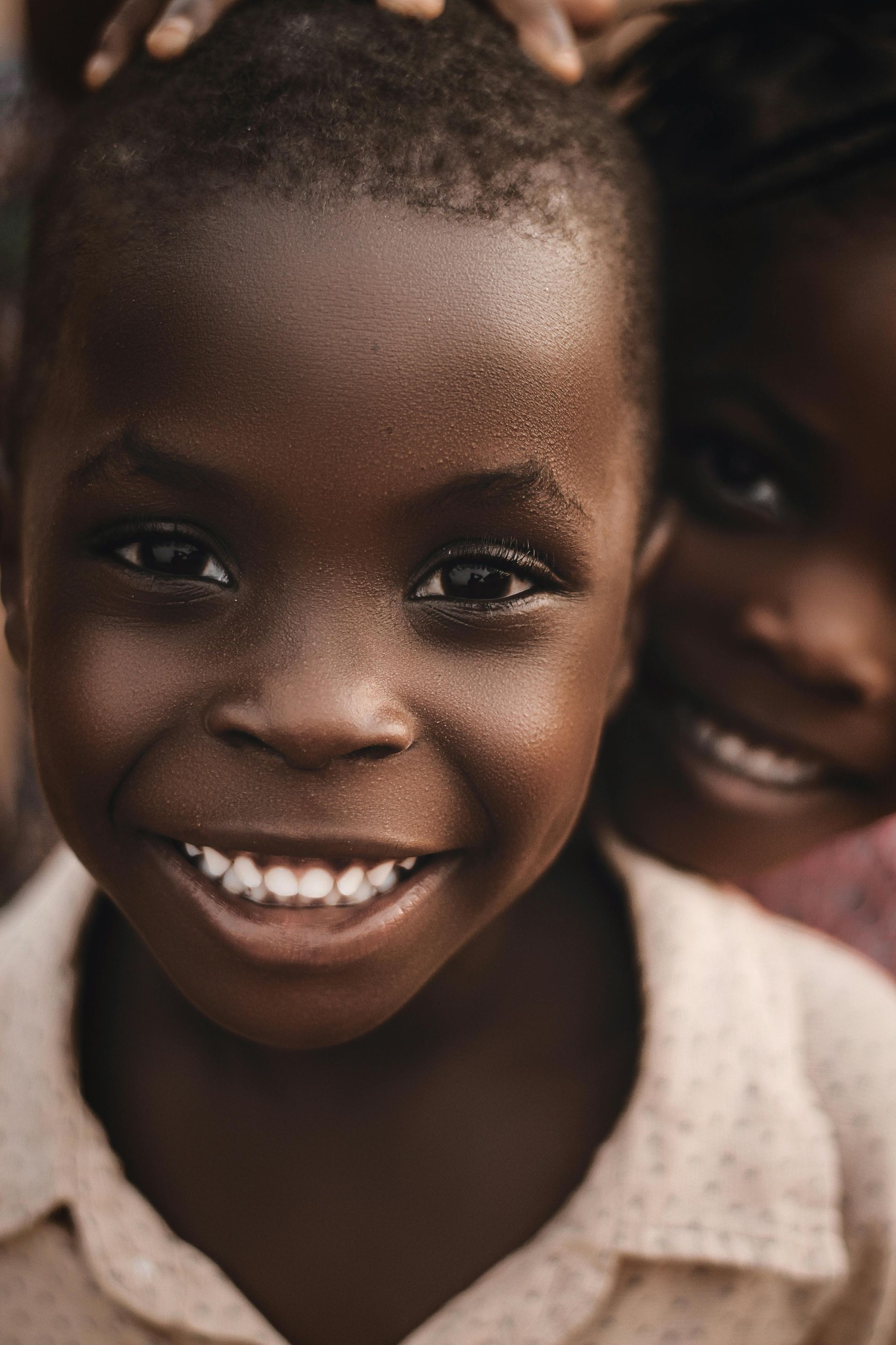 Two smiling children close together, one in front wearing a light shirt.