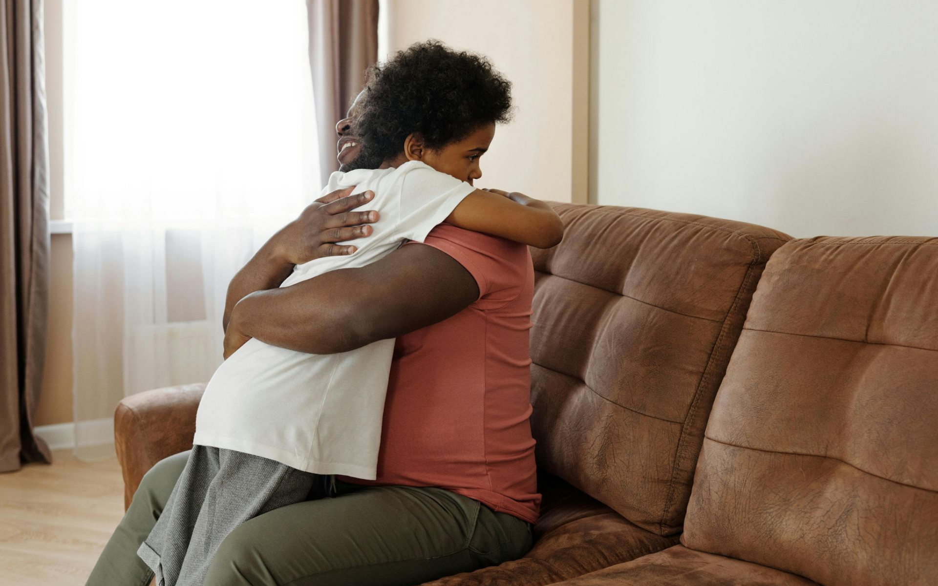 Father and son hugging on a brown couch in a bright living room