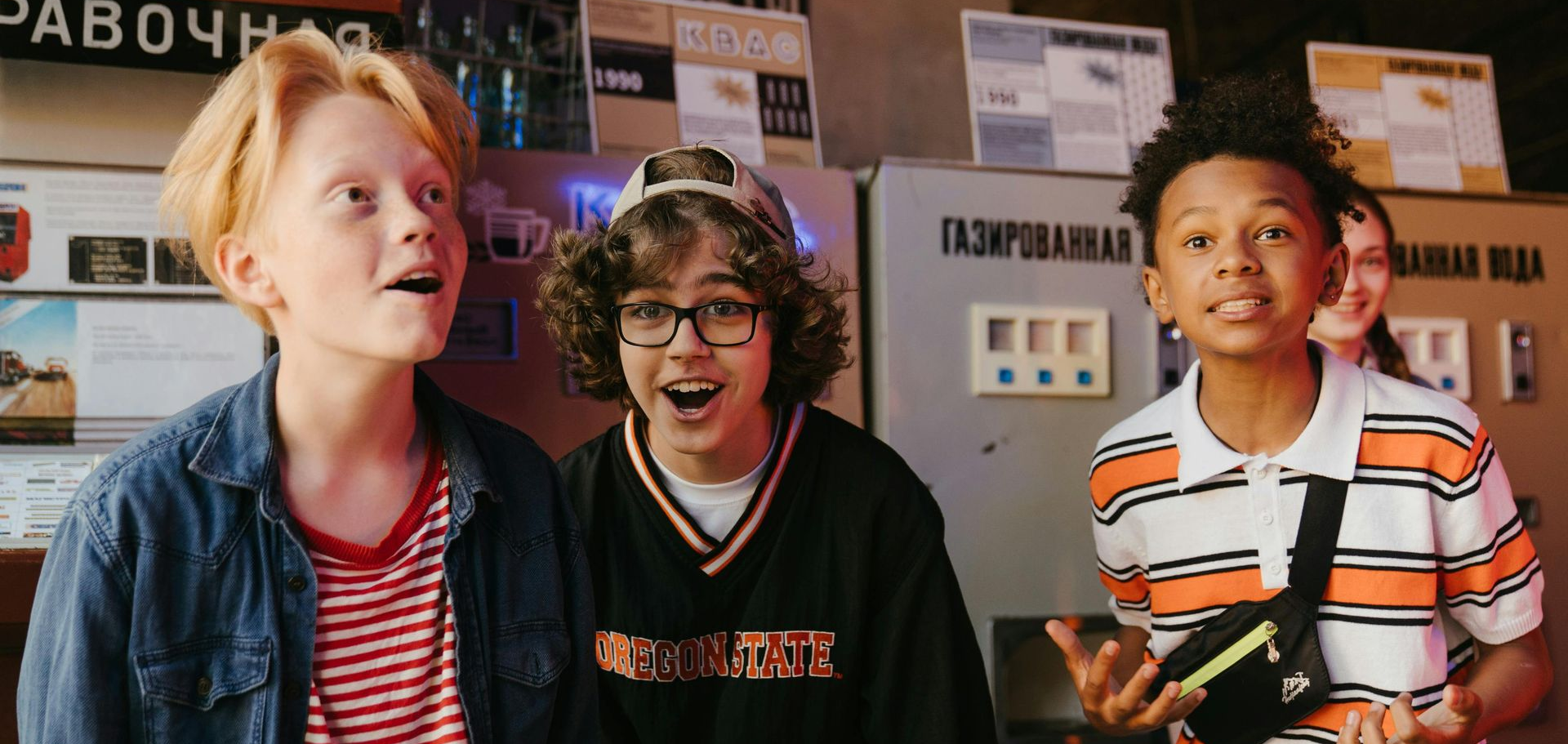Three smiling pre teen boys in front of a wall of posters and signs indoors