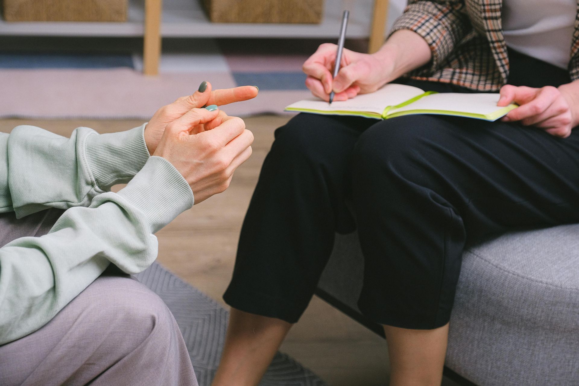 Two people discussing notes, one holding a pen over a notepad, seated on a sofa