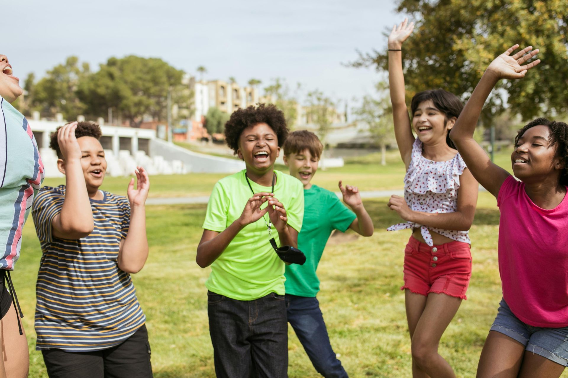 Children running and cheering together in a sunny park, smiling and raising their arms