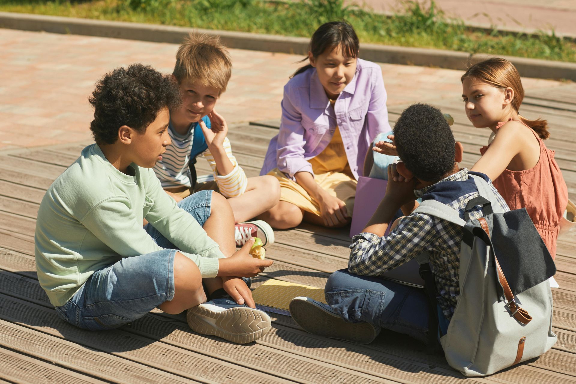 Children sitting in a circle outdoors on a wooden deck, talking and playing together