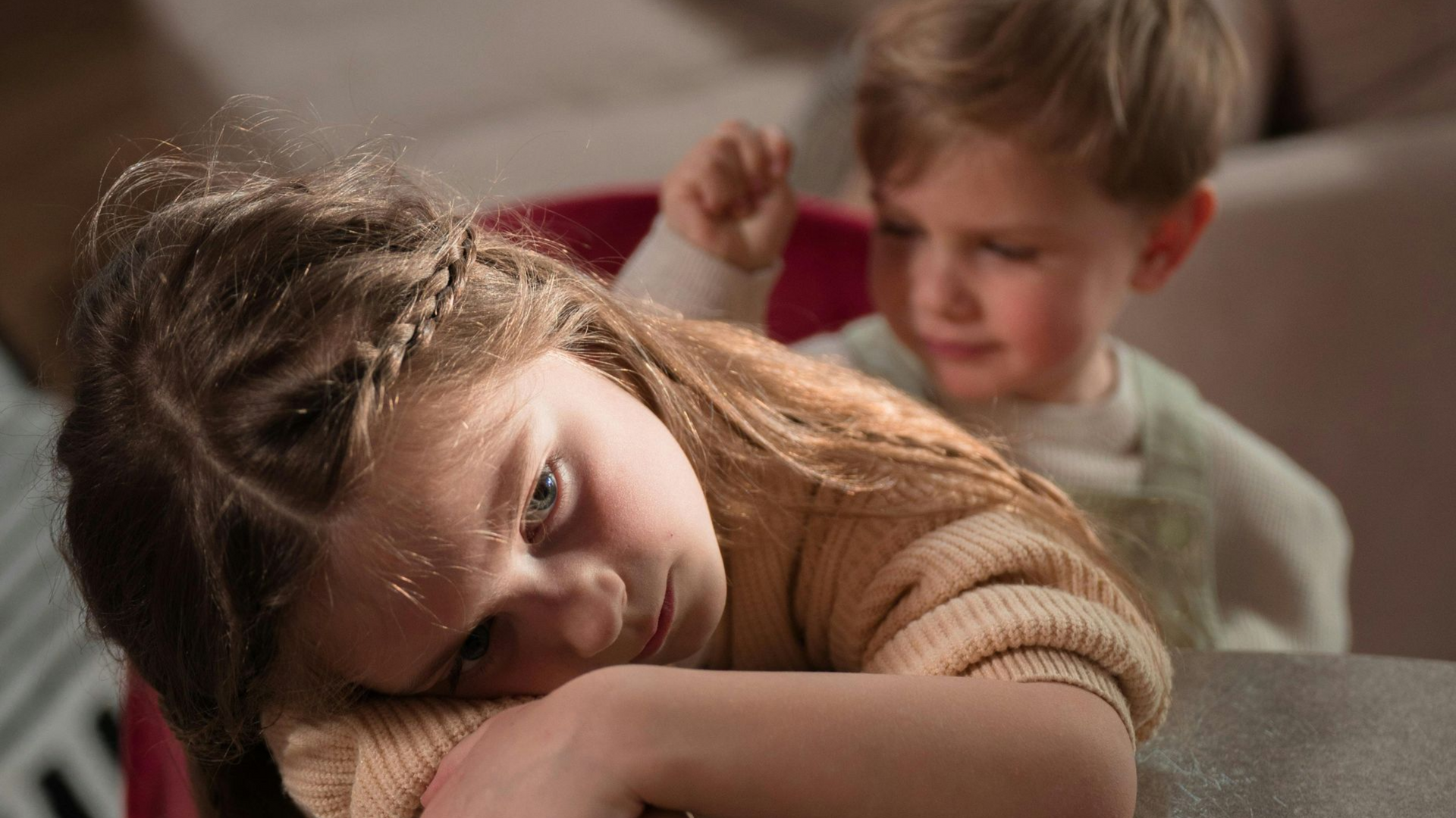 Sad child resting on a couch while another child reaches toward her from behind