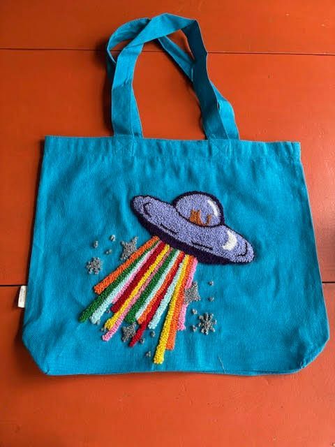 Turquoise draagtas met een paarse UFO die kleurrijke stralen uitstraalt en geborduurde sterren.