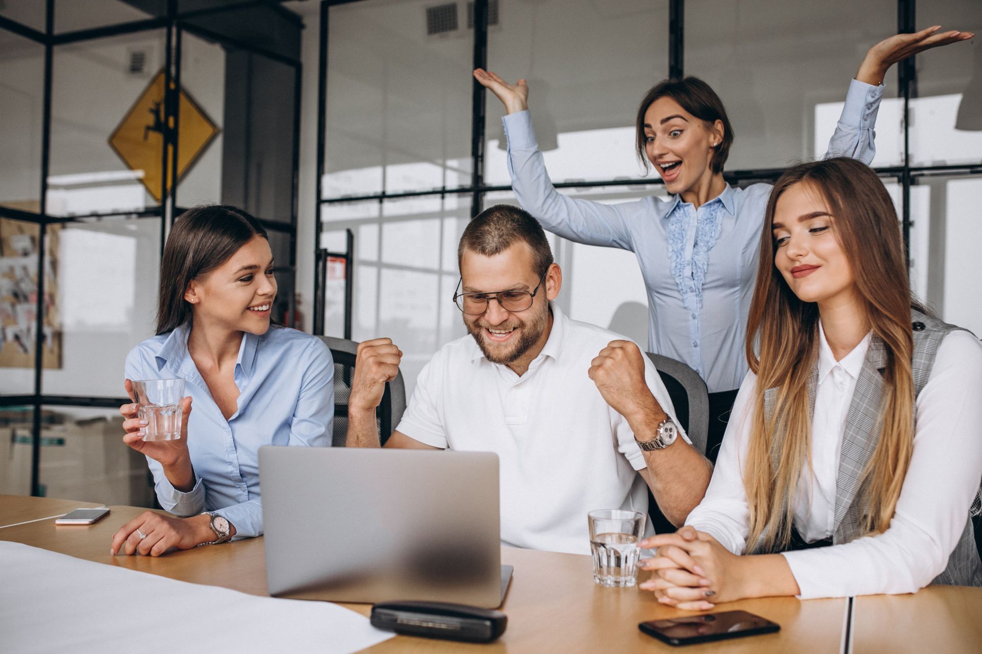 Colleagues celebrating around a laptop in a bright office meeting room