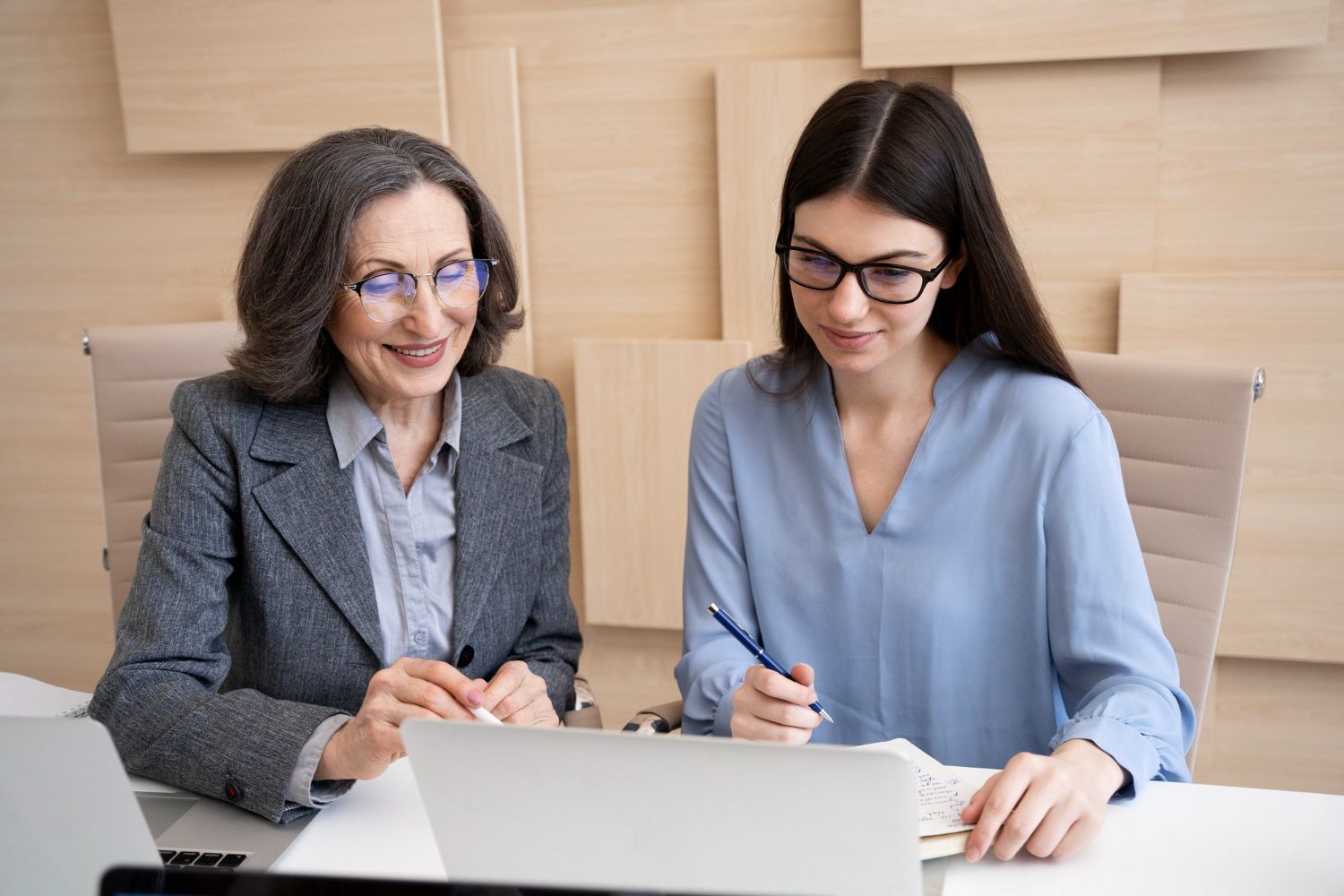 Two women in business attire reviewing a laptop and notes at a table