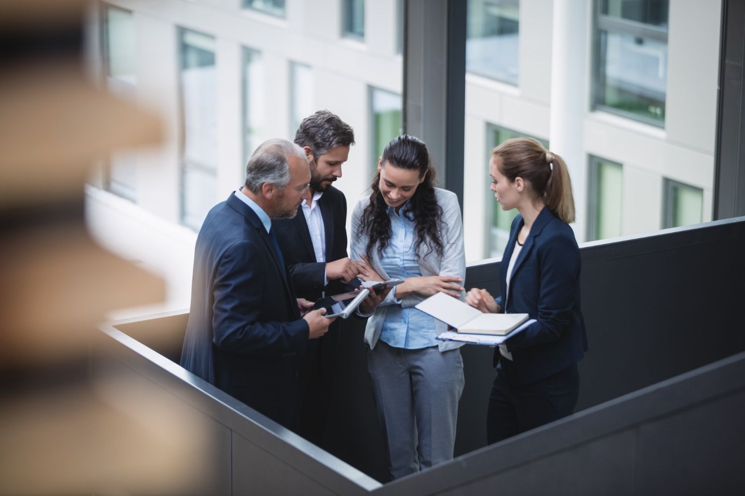 Four business professionals reviewing documents together on a balcony