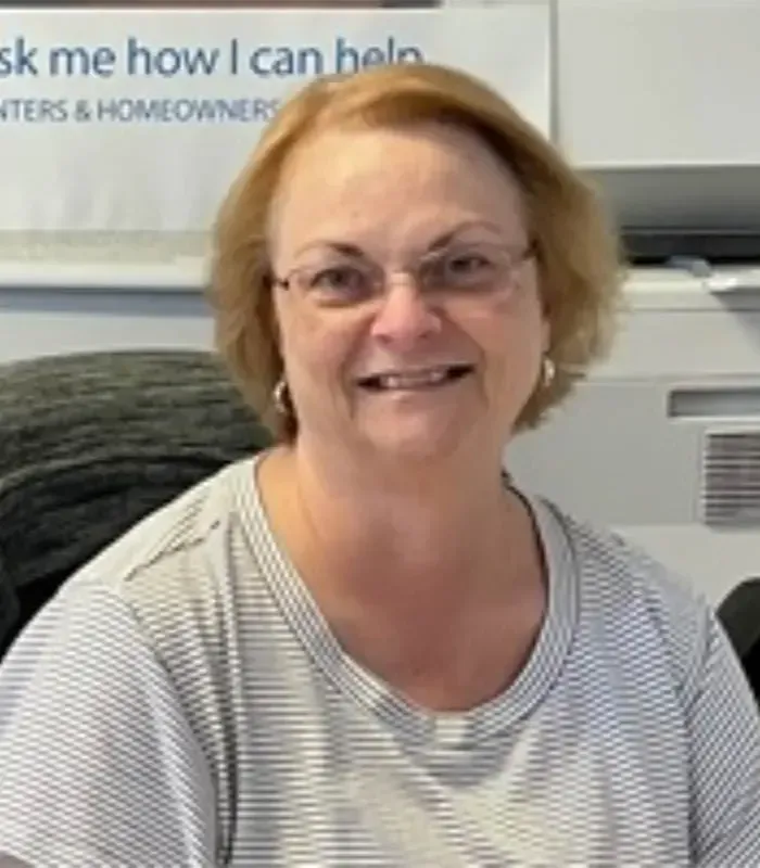 Smiling person in glasses and a striped shirt sitting indoors at a desk.
