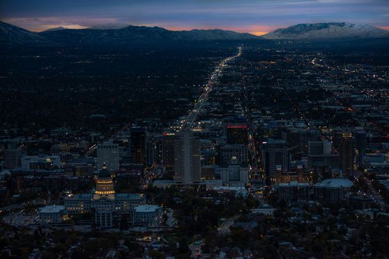 Dusk cityscape with glowing streetlights stretching toward dark mountains under a purple sky