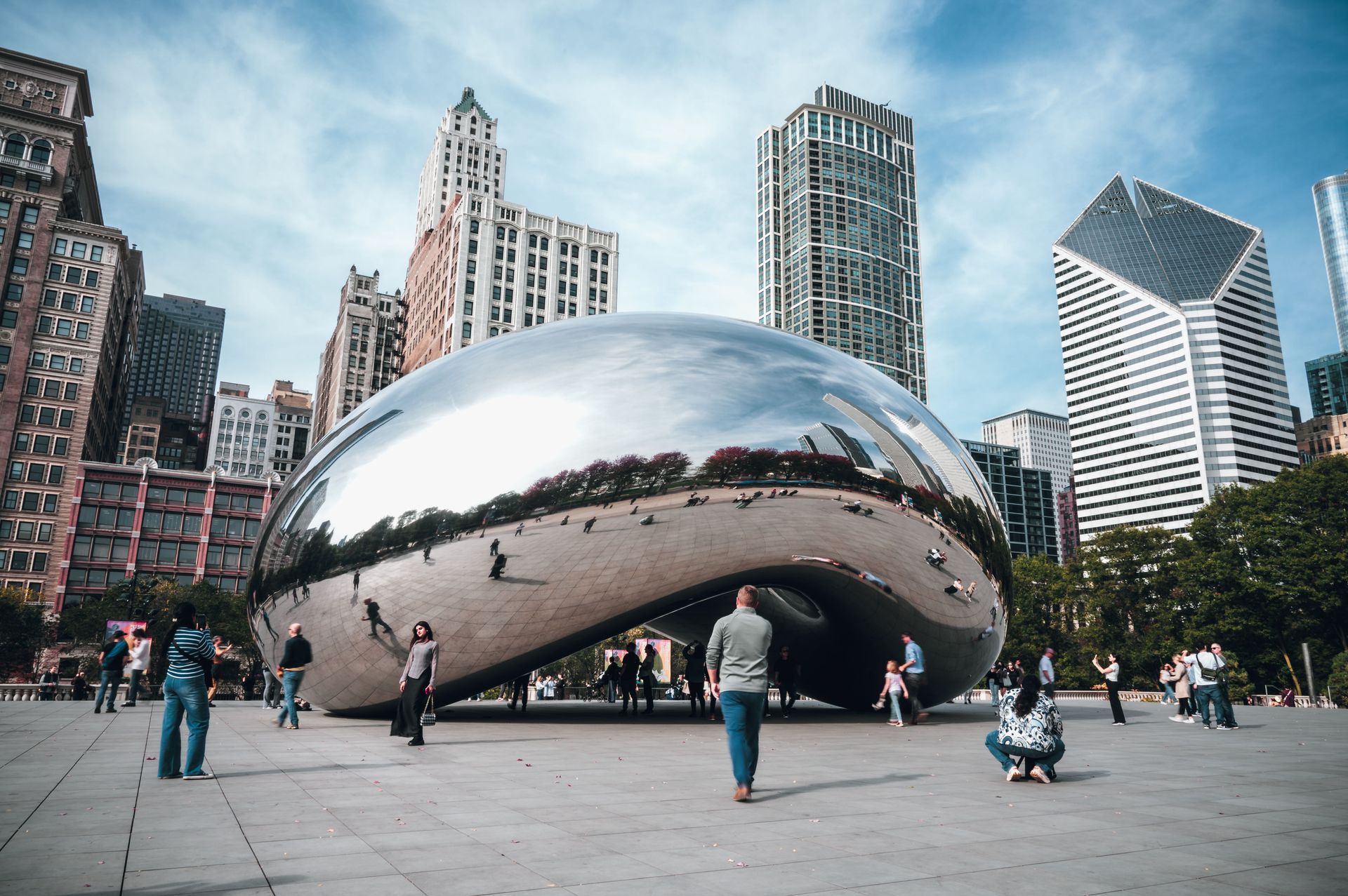 Cloud Gate sculpture in Chicago’s Millennium Park with people standing around it and city skyscrapers behind.