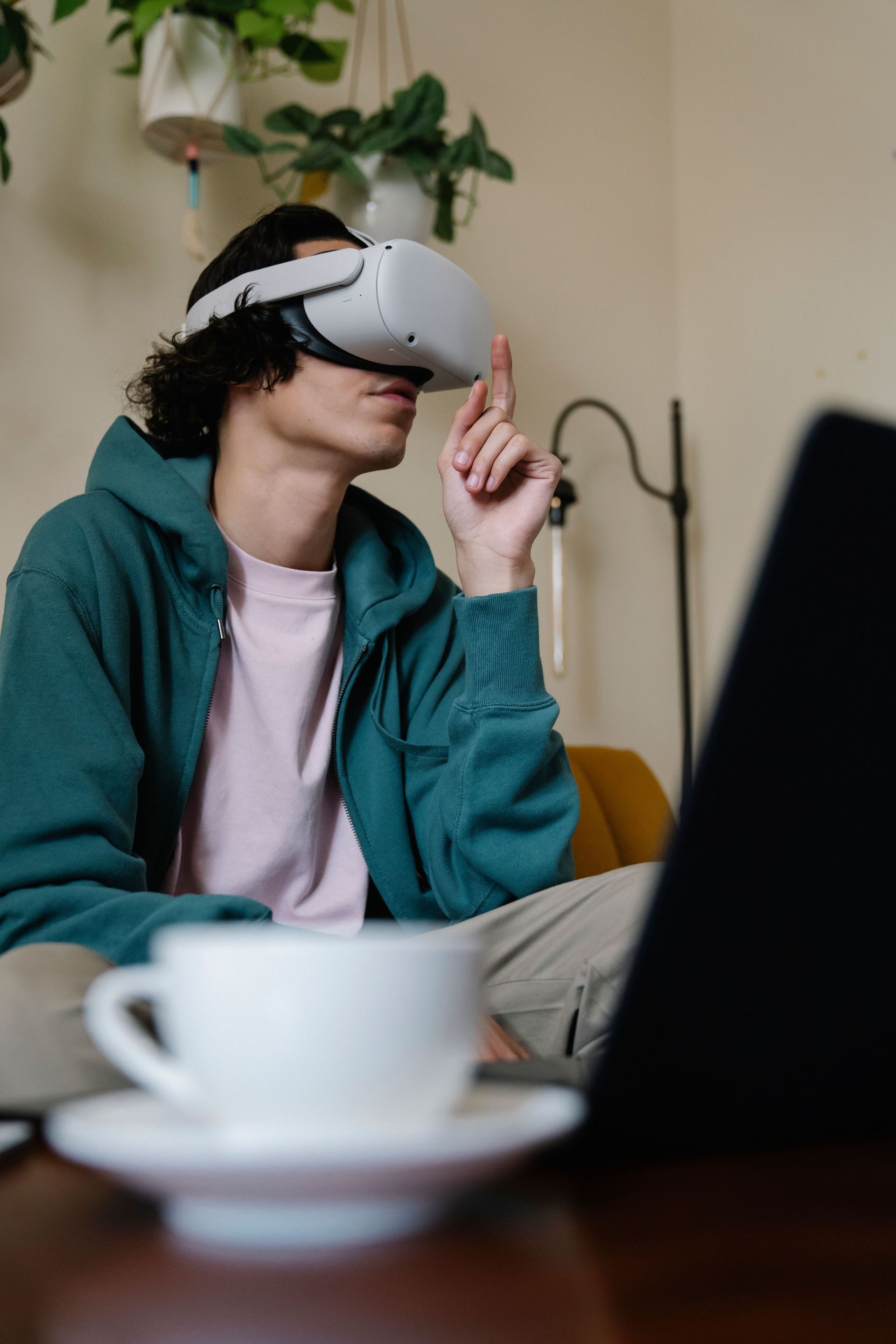 Person wearing a VR headset sits at a table with a laptop and coffee cup.