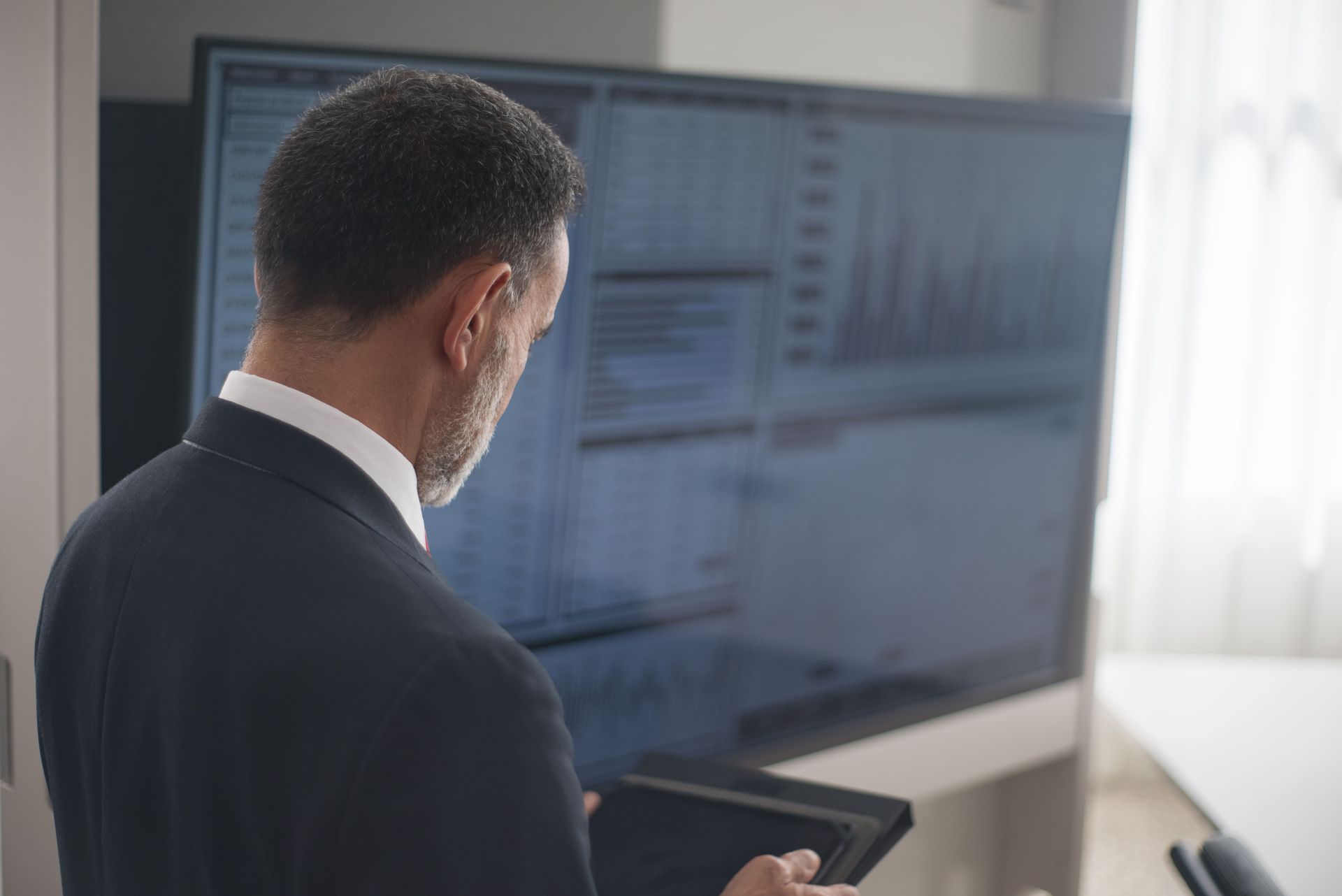 Person in a suit looking at a large computer screen in a bright office.