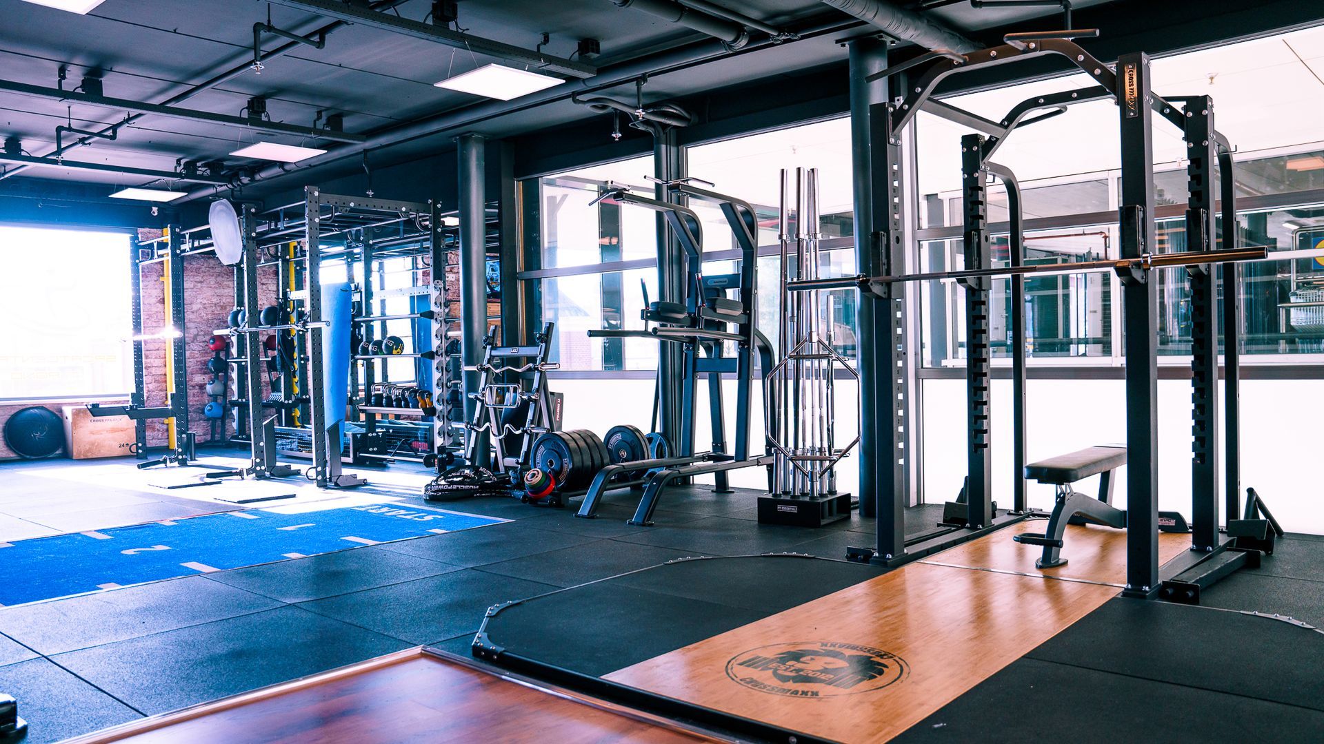 Interieur van een sportschool met gewichthefapparatuur: een power rack, halterstang, gewichten en een bank.