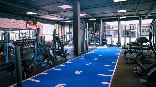 Interieur van de sportschool met apparatuur, waaronder gewichten en machines, en een blauwe trainingsbaan.
