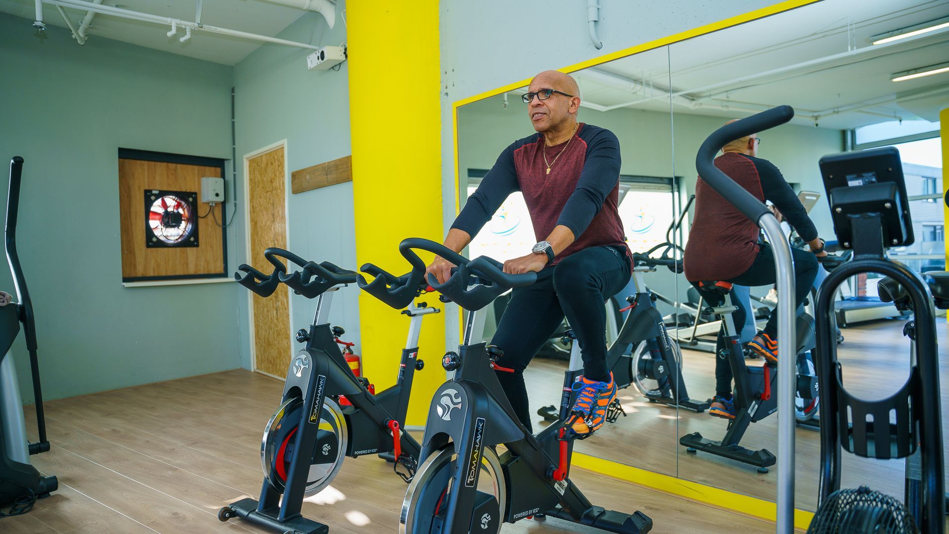Een man op een hometrainer, aan het trainen in een sportschool; zijn weerspiegeling in een spiegel.