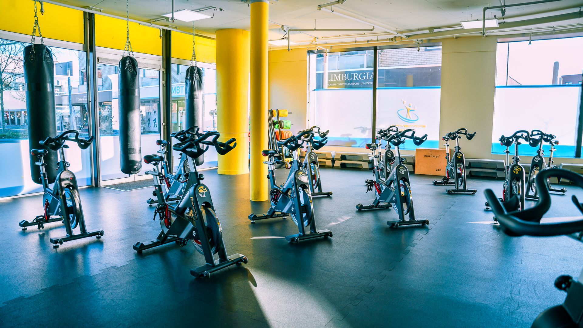 Spinningfietsen in een felverlichte sportschool met bokszakken.