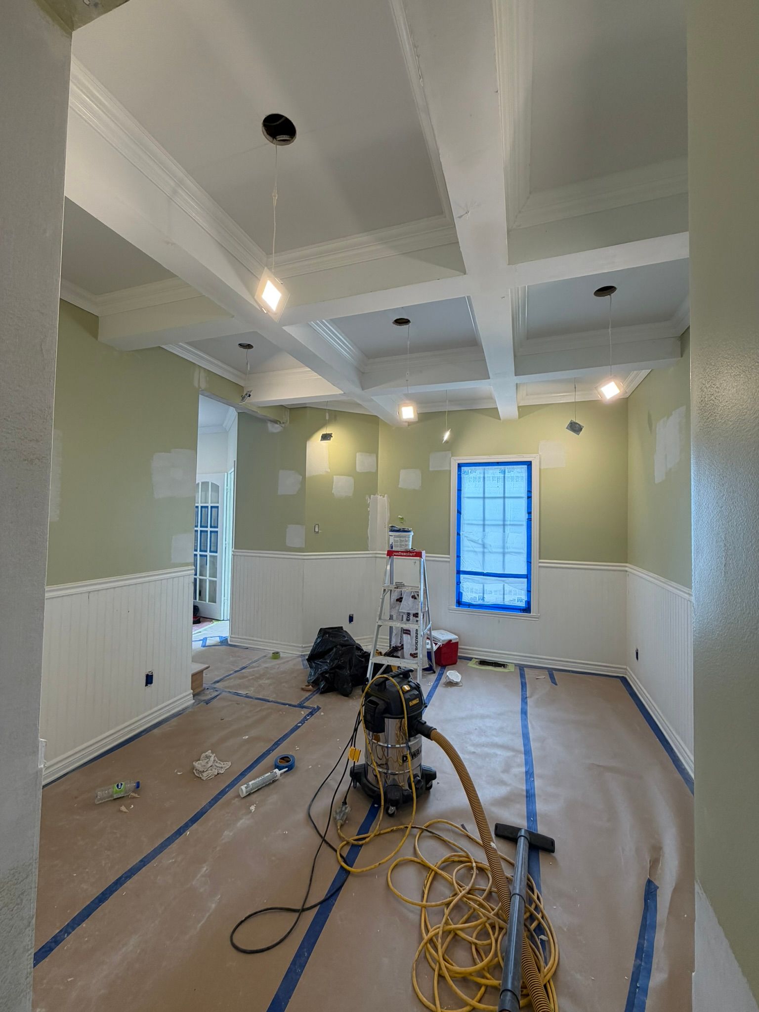 Renovated room with tools, cables, and supplies on the floor, white paneled walls, and a blue-framed window