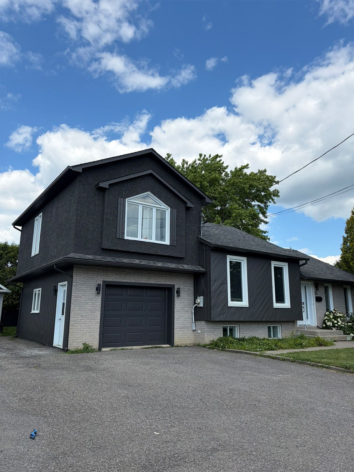 Black two-story house with garage, white-trimmed windows, and a paved driveway under a cloudy sky