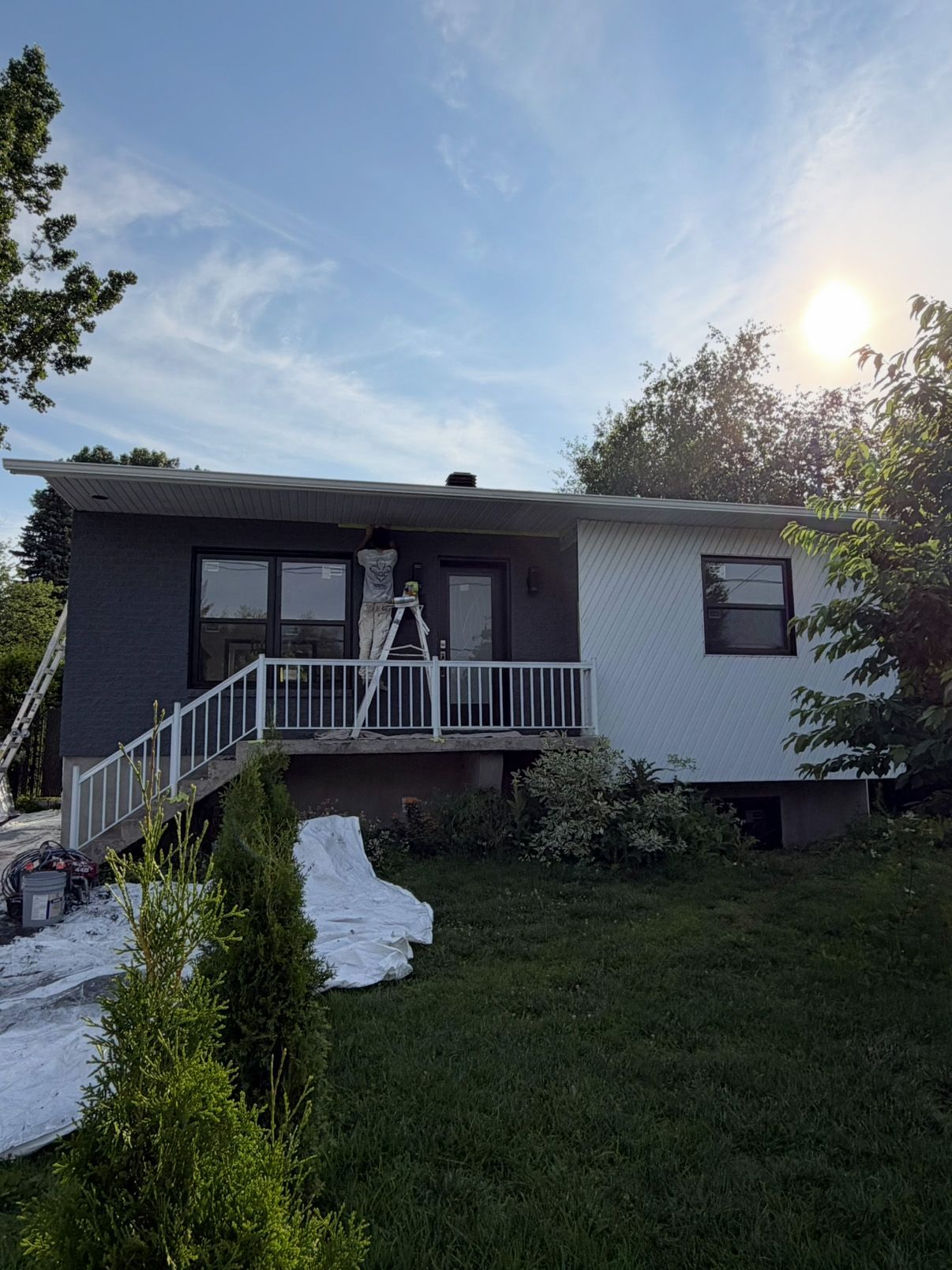 Single-story house at dusk with a front porch, steps, and a grassy yard, framed by trees and a bright sky