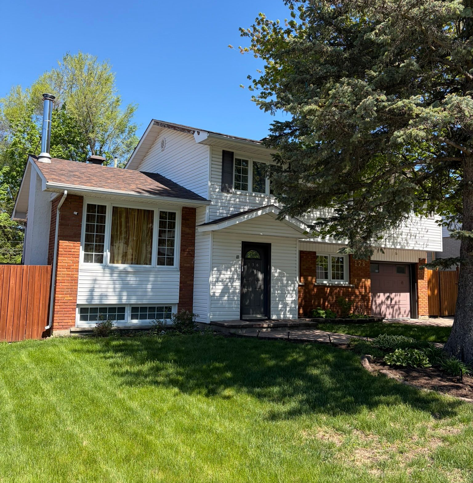 Two-story suburban house with white siding, red fence, and green lawn under a blue sky