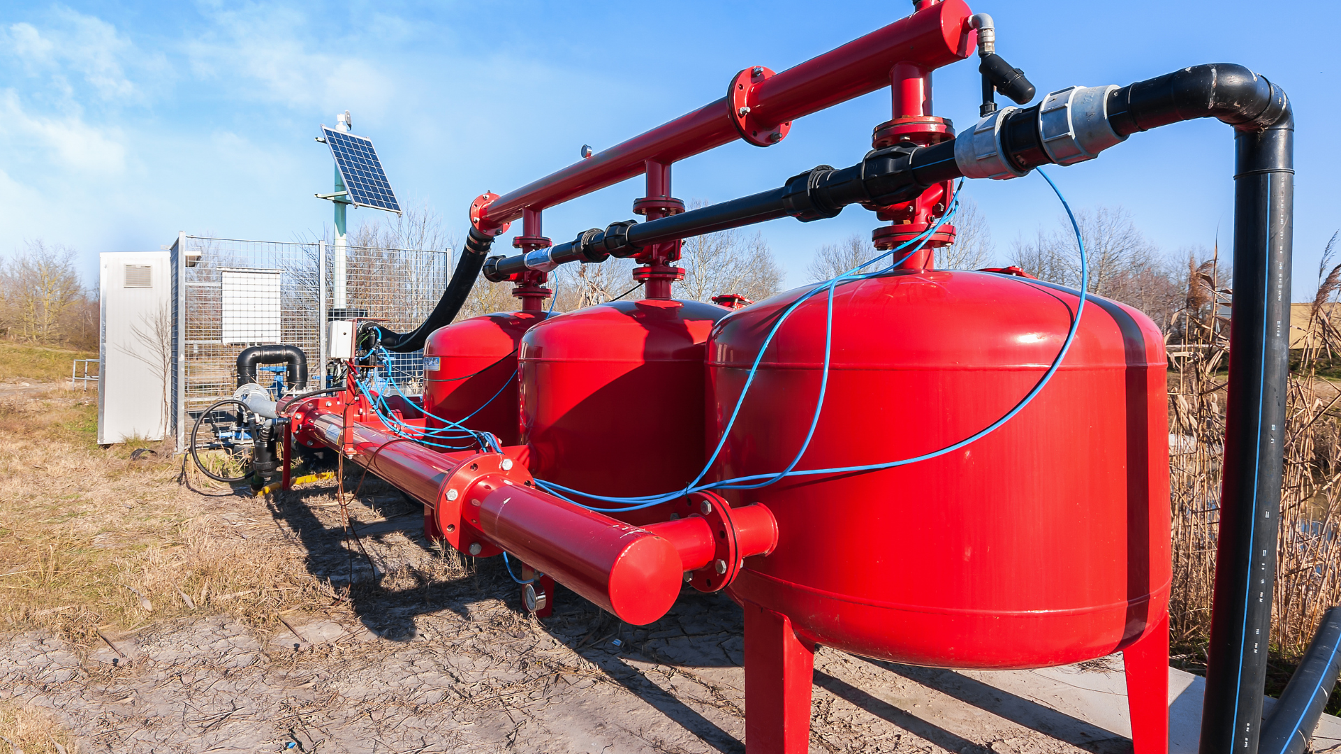 Sistema de filtración de agua roja en ambiente exterior, con tuberías, tanques y panel solar.