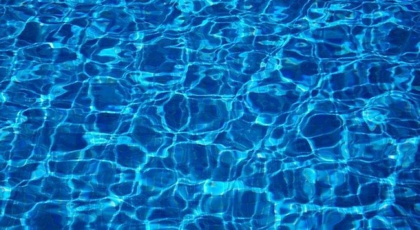 Agua de piscina azul ondulada, luz del sol reflejándose en la superficie.