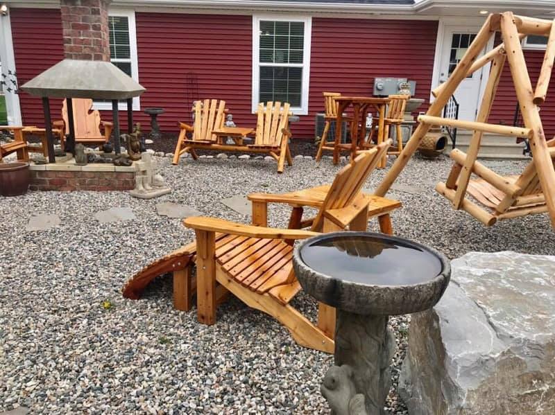 Outdoor seating area with wooden furniture, stone bird bath, and red siding.