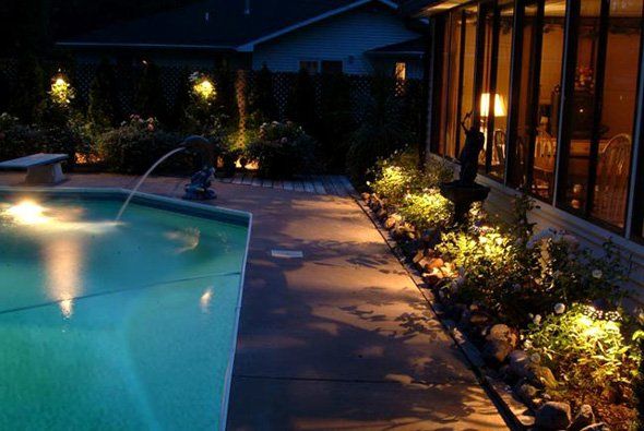 Poolside garden at night, illuminated by pathway and accent lights.