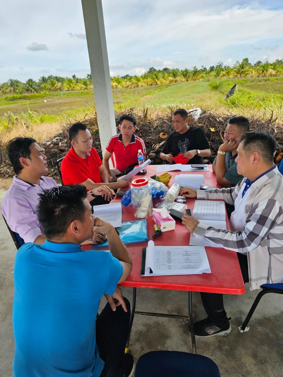 A group of men are sitting around a table in a field.