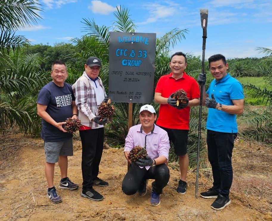 A group of men are posing for a picture in a field holding palm nuts.