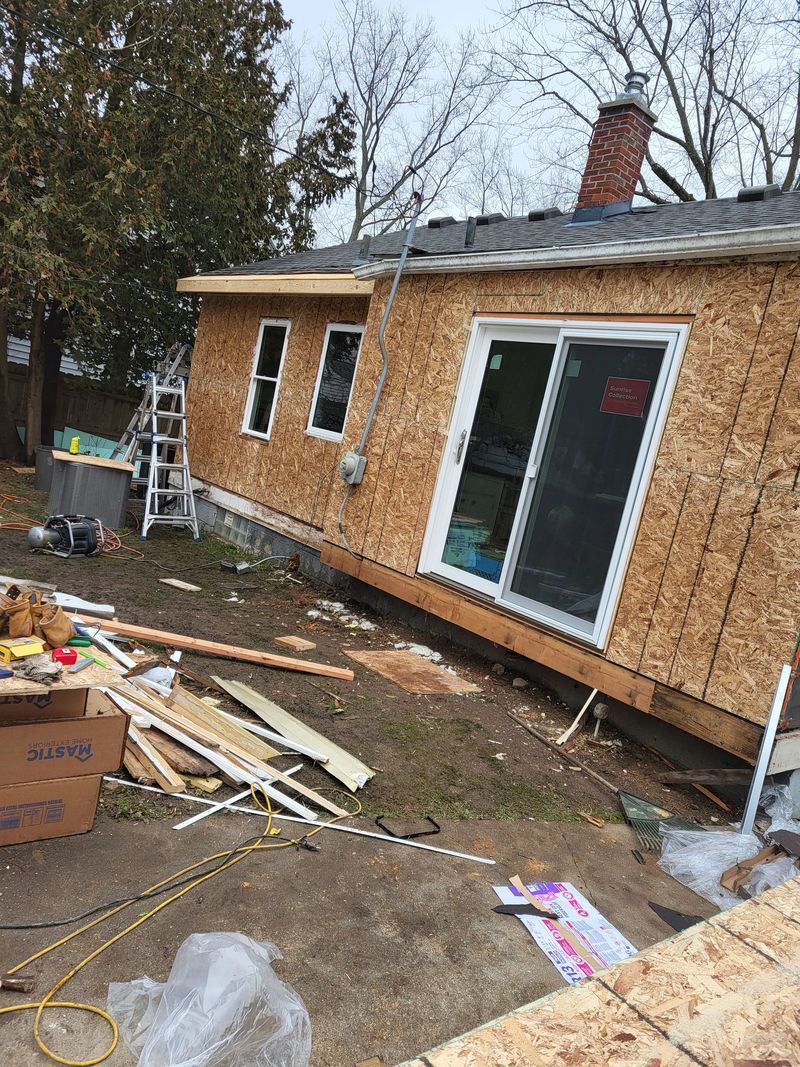 House exterior under construction with exposed wood sheathing. Sliding glass door and windows installed.