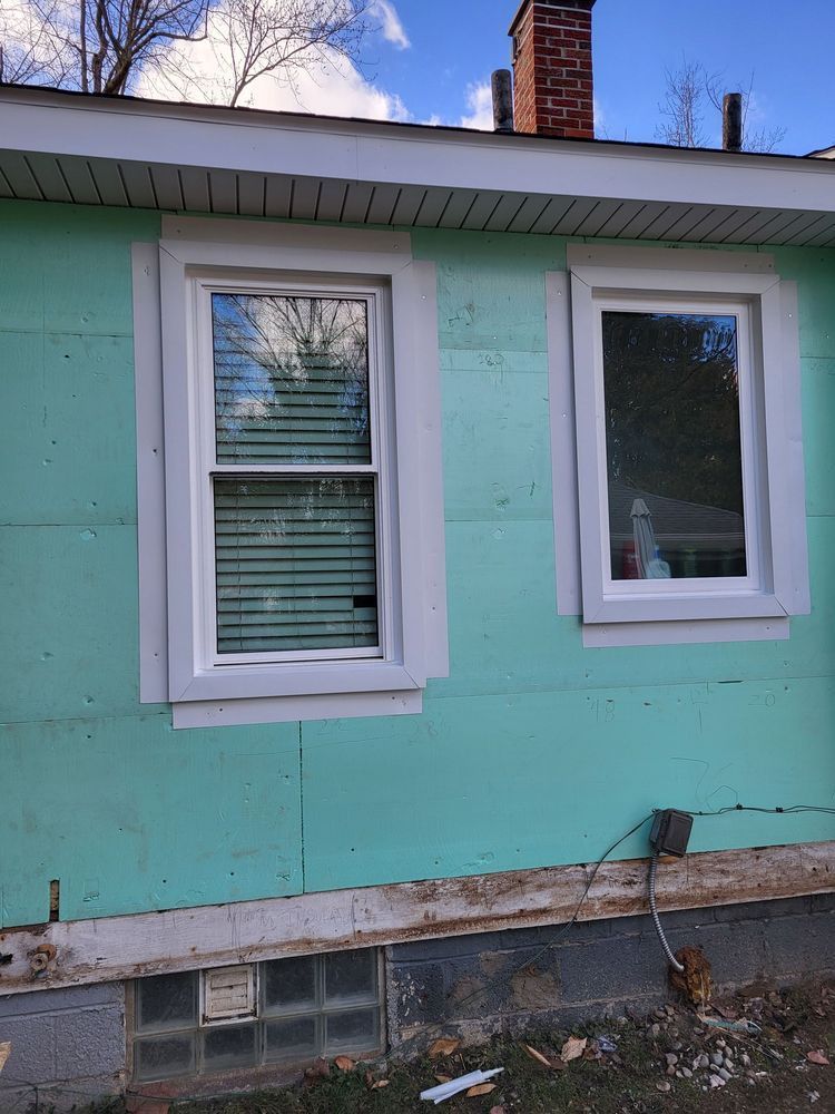 Two white-framed windows on a teal wall with insulation showing. A brick chimney is visible.