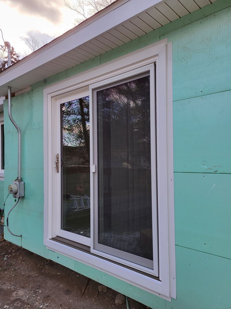 White-framed sliding glass door on a teal-colored building with a gray electrical box next to it.