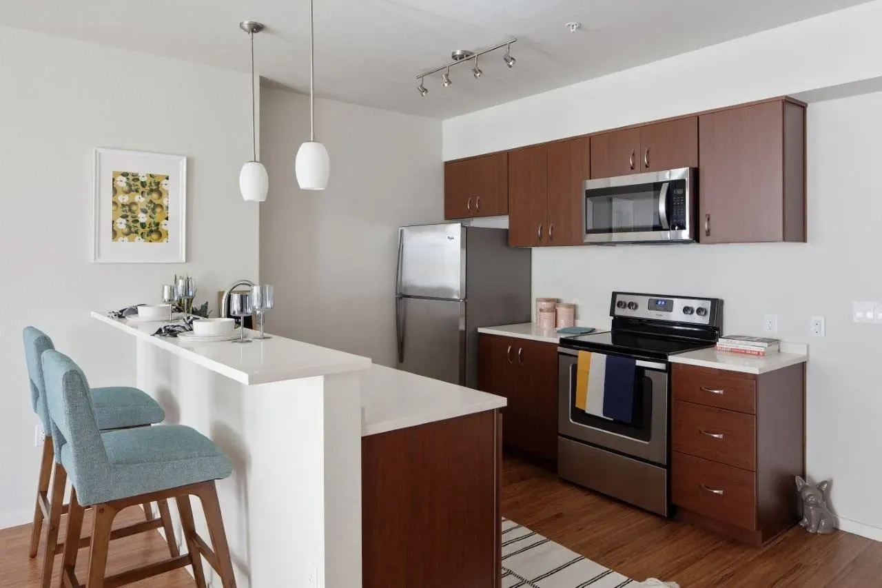 Modern kitchen with stainless steel appliances, wood cabinets, and a breakfast bar with pendant lighting.
