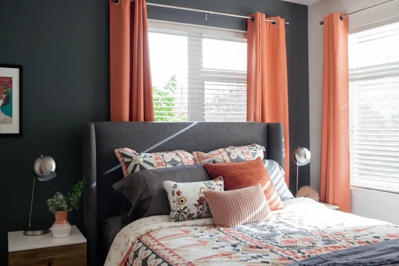A stylish bedroom featuring a king-size bed with patterned bedding and coral curtains.
