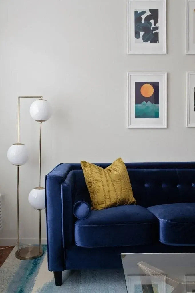 A blue velvet sofa with a mustard yellow throw pillow and abstract art on the wall.