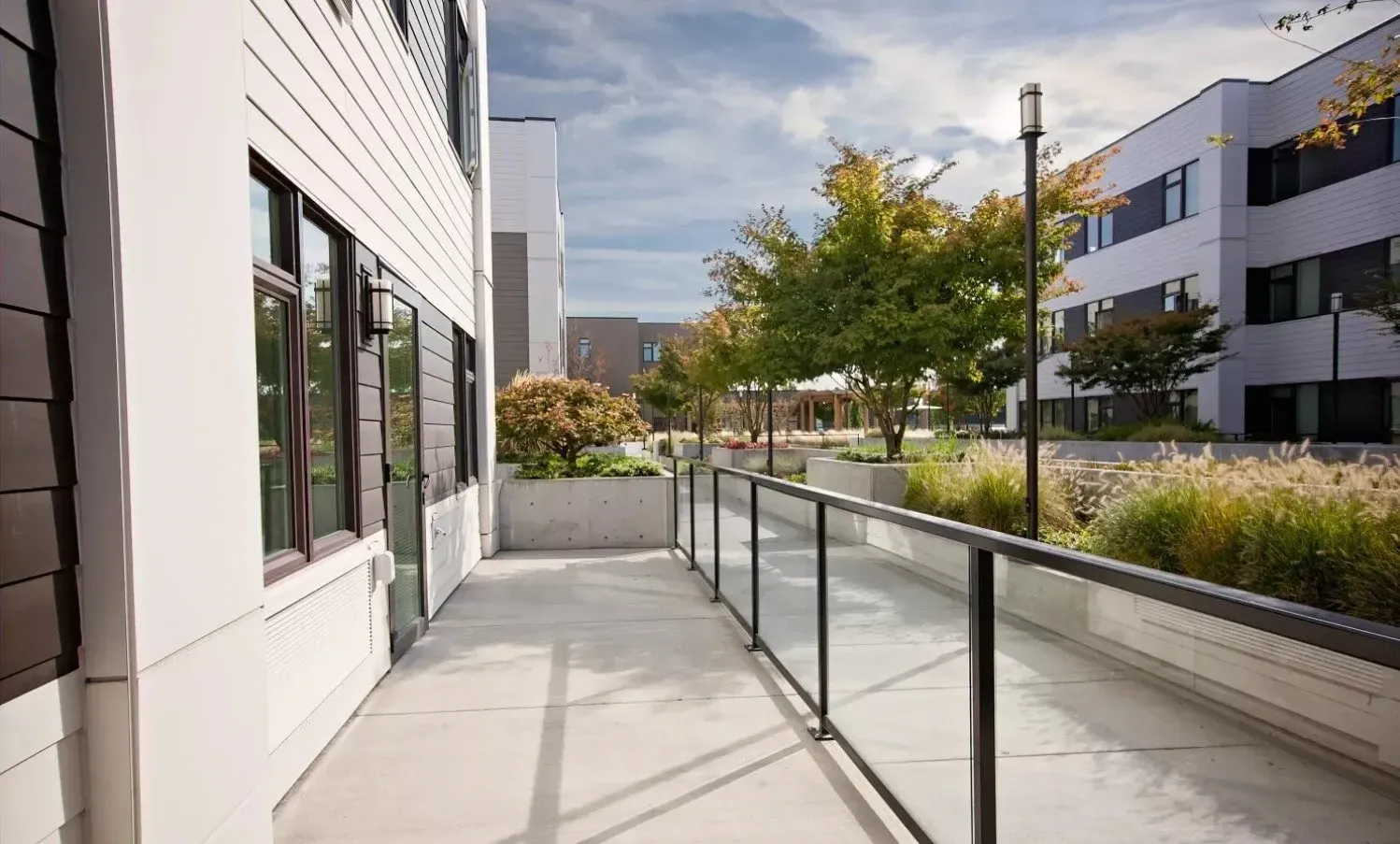 Outdoor walkway with glass railings overlooking a landscaped courtyard with trees and benches.