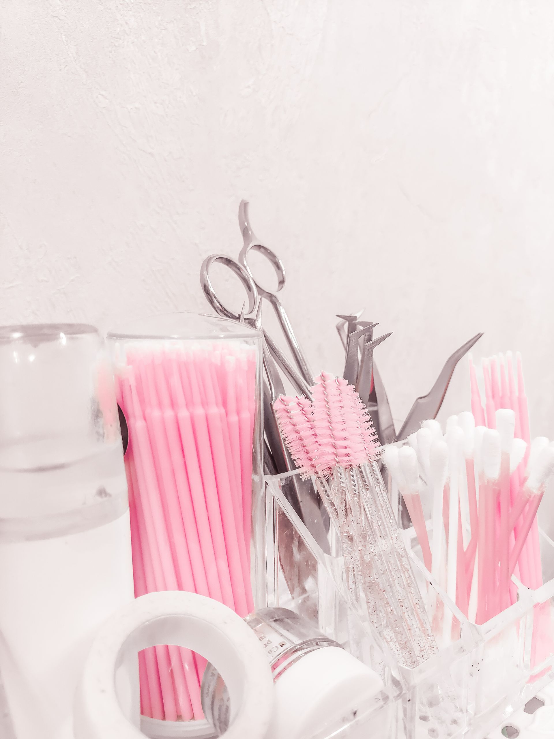 Pink and white disposable dental tools in containers, with a pair of scissors on a white surface